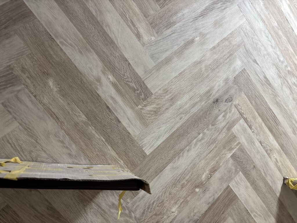 Completed herringbone-patterned wallpaper covering a wall in a renovated hotel room.