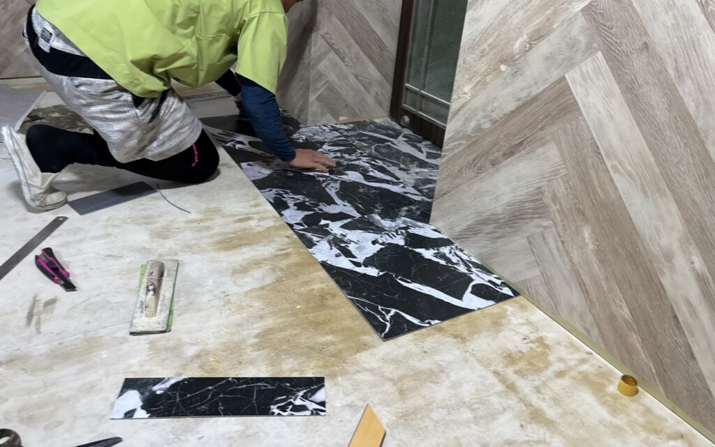 A worker cutting and fitting a vinyl floor tile before applying adhesive during hotel renovation.