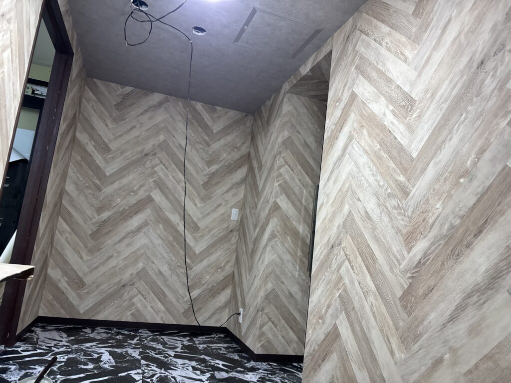 Wide view of a completed hotel room interior with new wallpaper, vinyl floor tiles, and soft baseboards.
