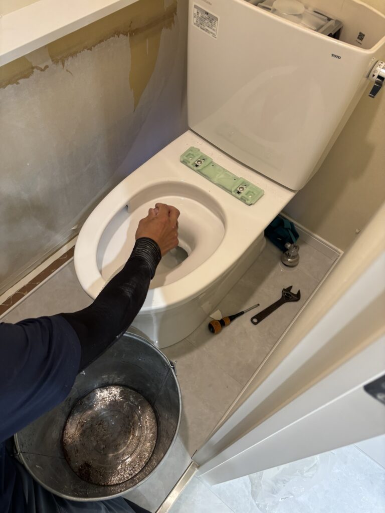 Using a manual hand pump to drain water from a toilet bowl into a bucket