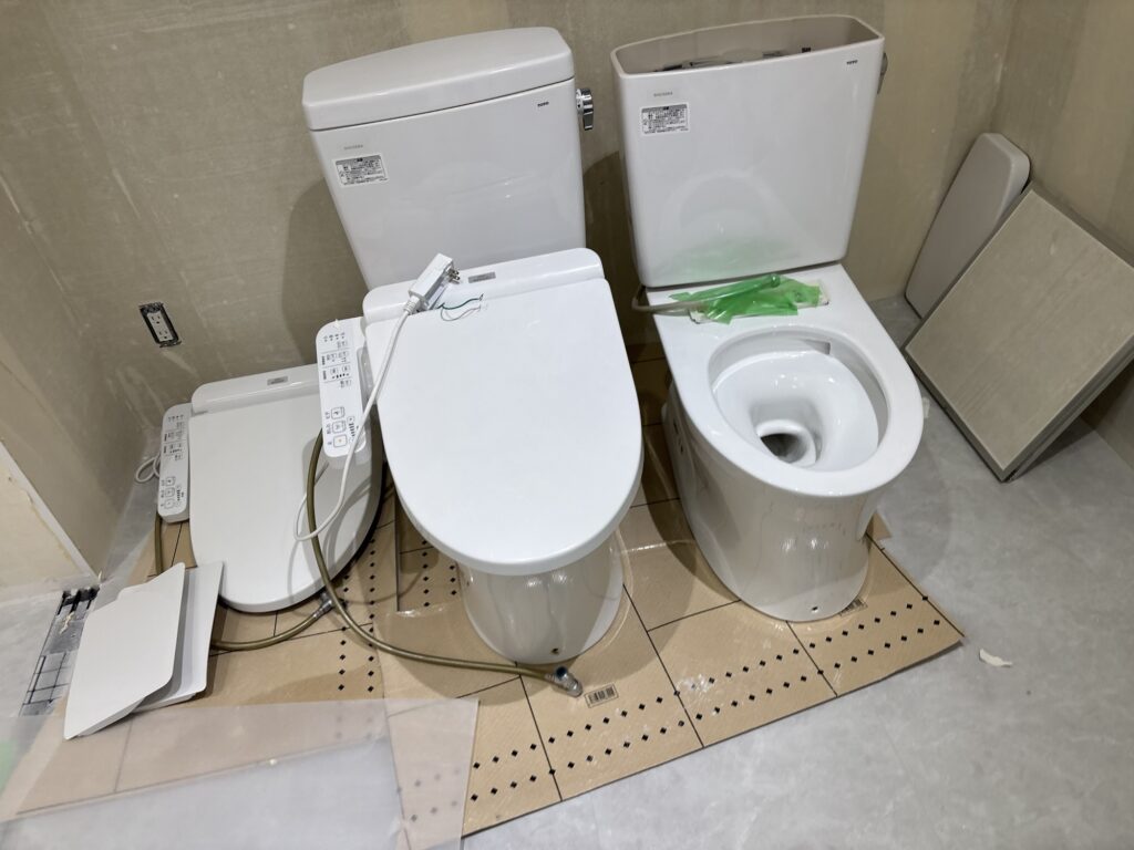 Two toilets removed from a commercial bathroom before floor tile installation