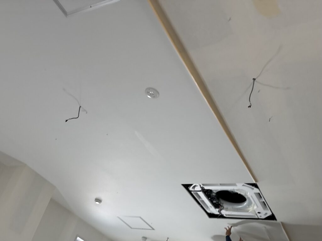 Worker installing thin white wallpaper on a commercial ceiling.