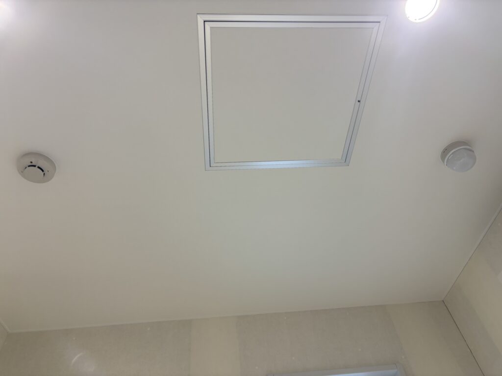 White ceiling wallpaper neatly cut around an inspection hatch and alarm device.