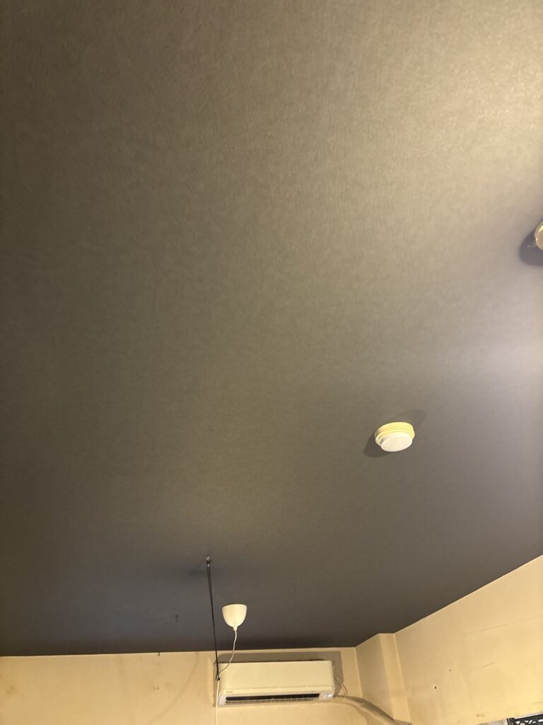 Finished living room ceiling featuring newly installed black wallpaper.