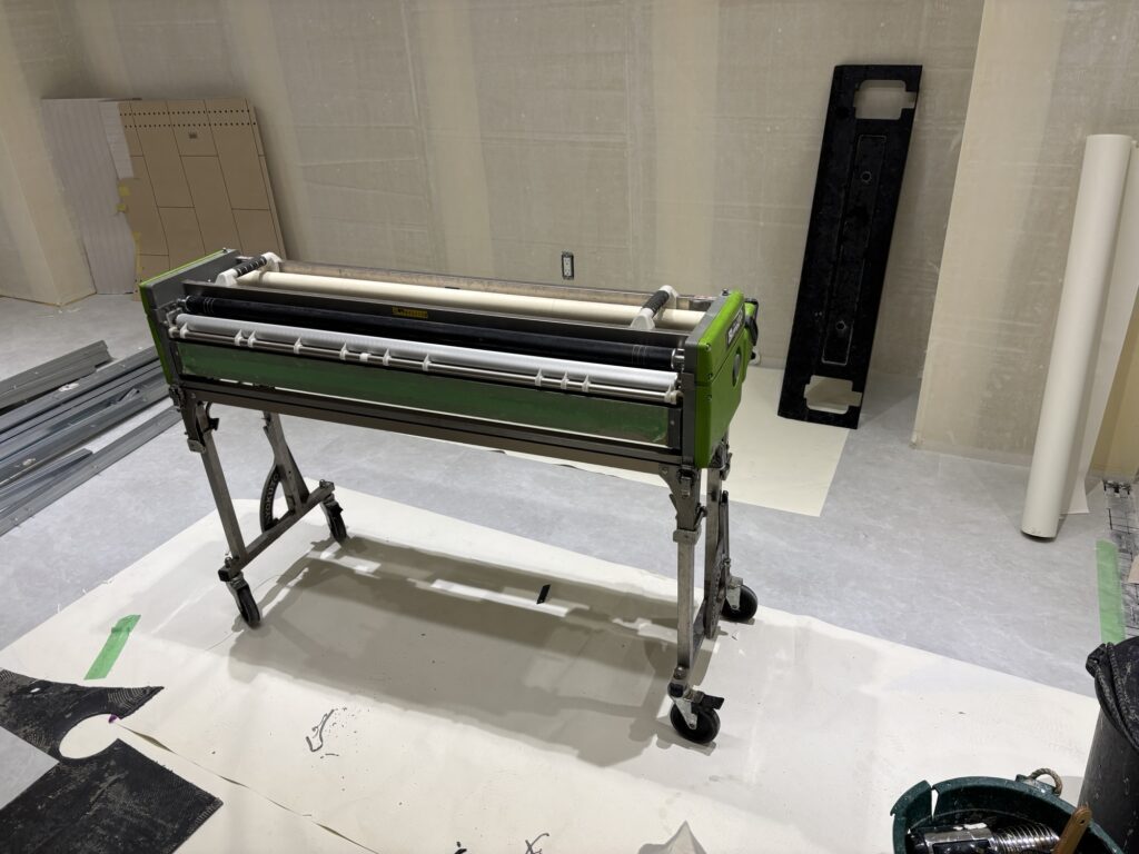 Wallpaper passing through a wallpaper pasting machine to apply adhesive before installation at a commercial renovation site in Tokyo, Japan.