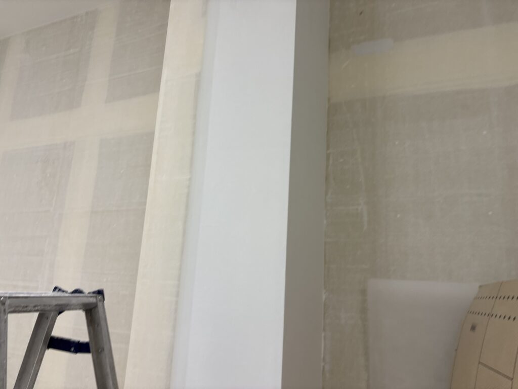 A wallpaper installer carefully applying wallpaper around a column during commercial restoration work in Tokyo, Japan.