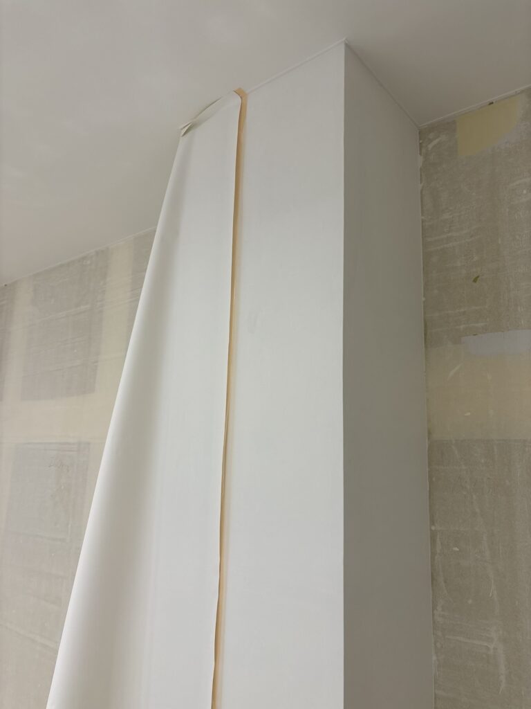 Partially installed wallpaper being pressed and smoothed around a column to create a clean, straight corner.