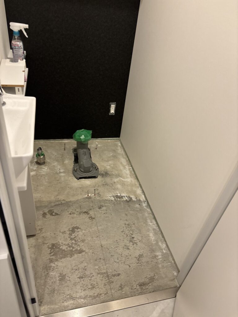 Toilet floor with the existing tiles removed, exposing the underlying surface before the new flooring installation.