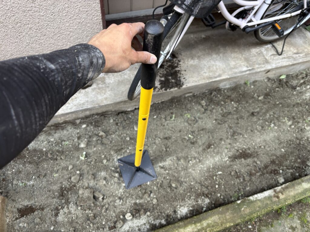Manual hand tamper used to compact soil treated with soil stabilizer during DIY ground preparation.