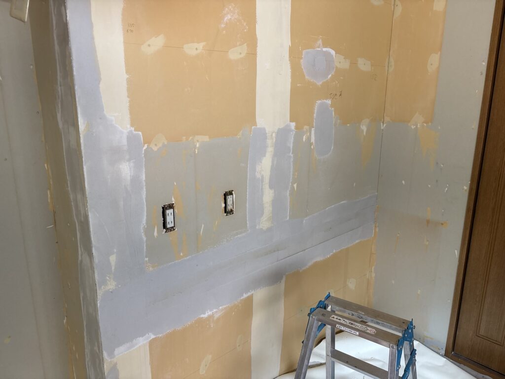 Kitchen wall with the first coat of joint compound applied during surface preparation for new wallpaper.