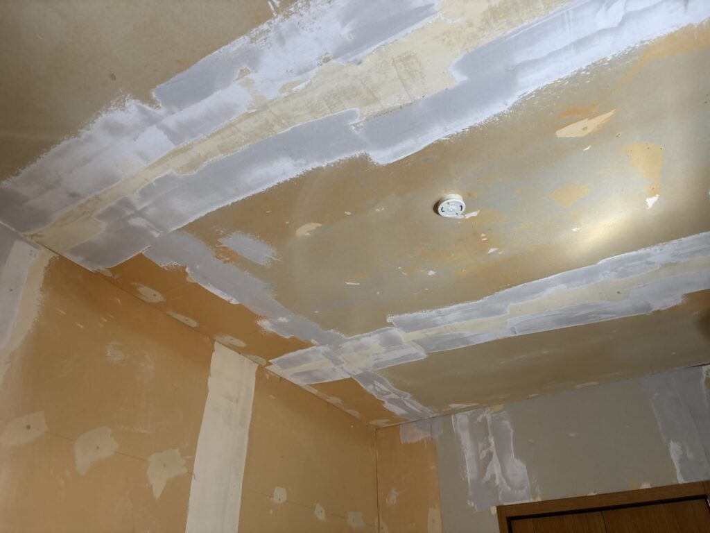Kitchen ceiling with the first coat of joint compound applied during preparation for wallpaper installation.
