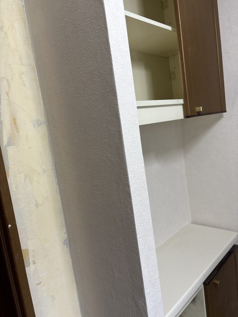 Finished wallpaper installation on a column beside a cabinet in a washroom.