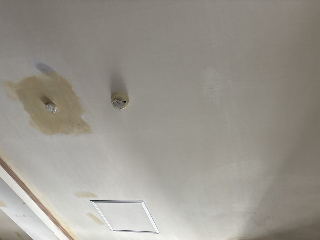 Repaired ceiling and wall areas covered with finishing compound before new wallpaper installation.