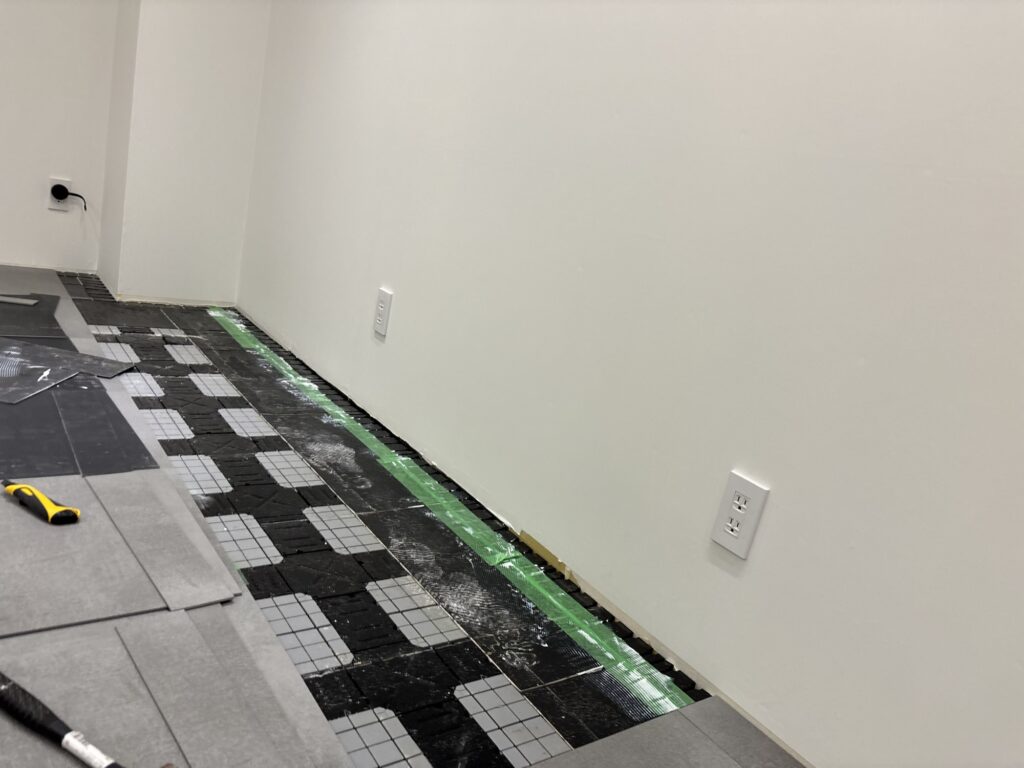 Worker adjusting a raised access floor panel before installing a narrow vinyl tile along the wall.