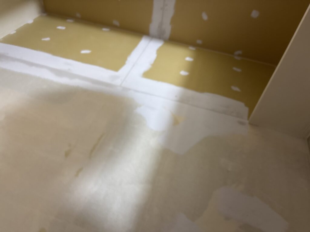 Base coat putty applied to the toilet walls and ceiling before wallpaper installation.
