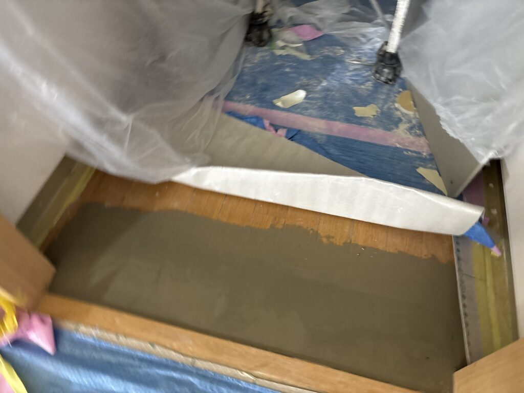 Putty applied to an uneven area of the kitchen floor before new cushion flooring installation.