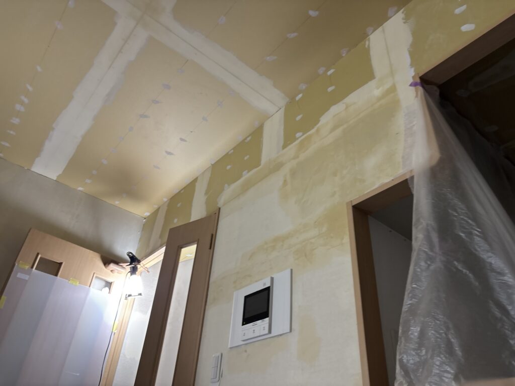Living room walls and ceiling covered with finish coat putty in preparation for wallpaper installation.
