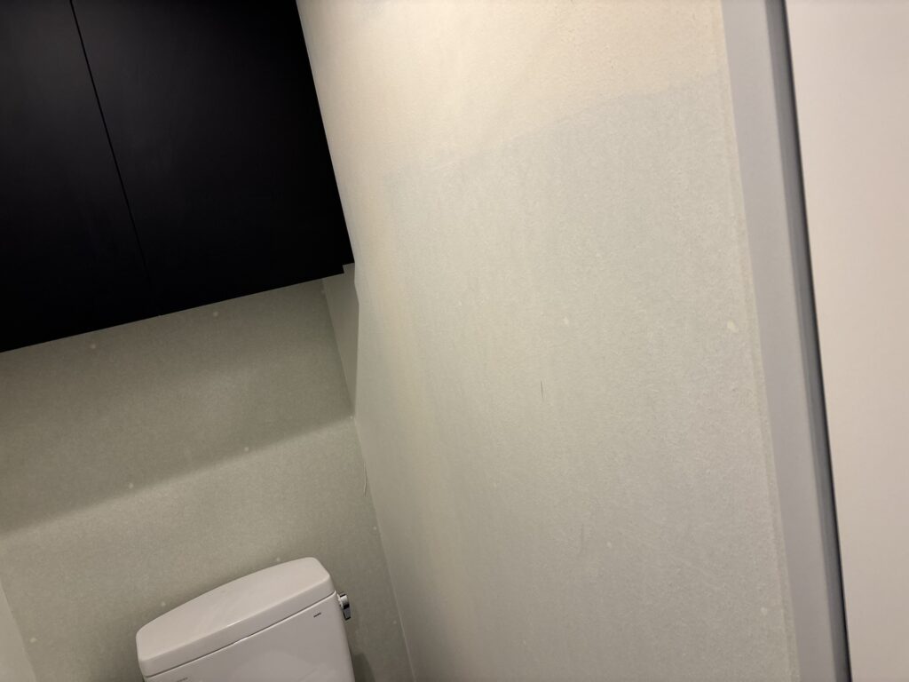 Toilet interior in a commercial building in Japan before wallpaper installation, showing the existing wall and ceiling surfaces.