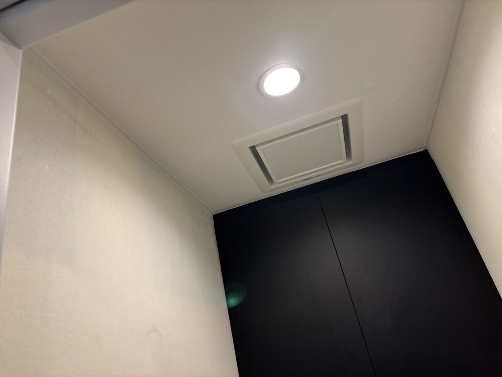 Completed white wallpaper installation on a toilet ceiling, including the area around the ventilation fan opening.