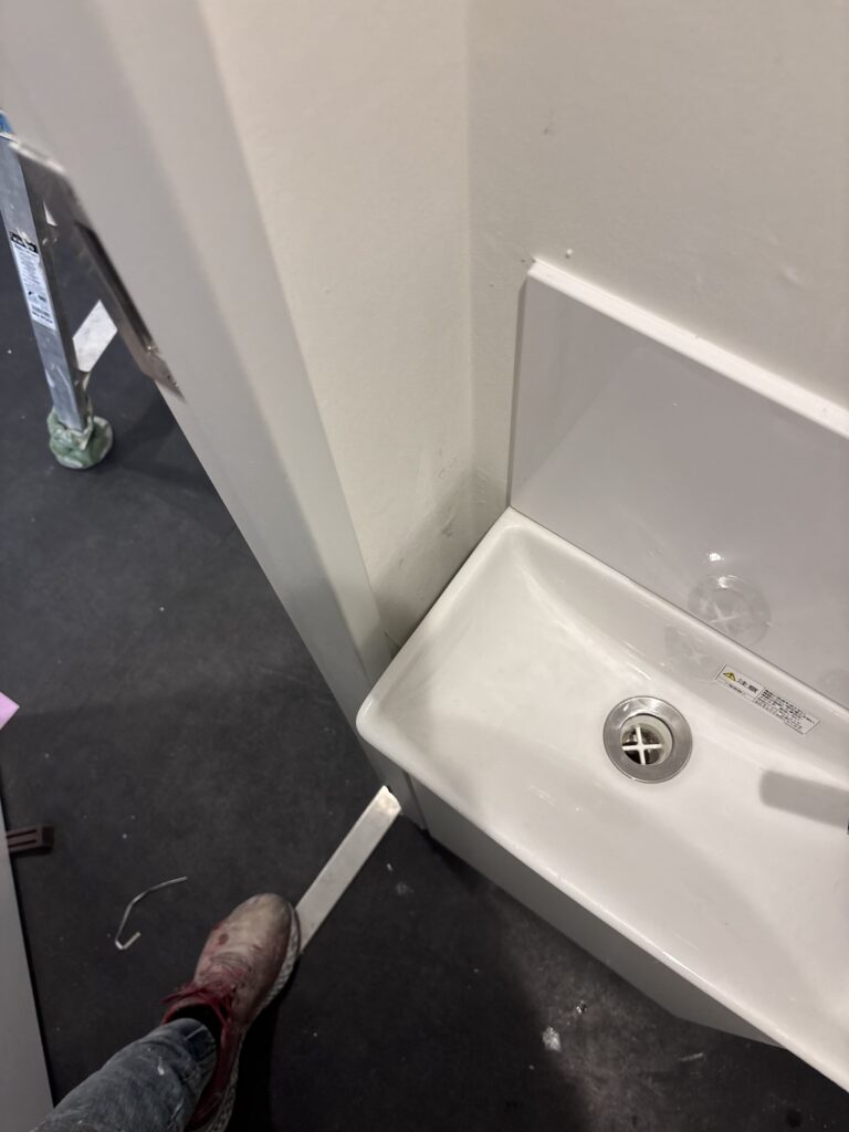 Newly installed wallpaper fitted into a narrow space beside the plumbing fixtures in a commercial toilet renovation.