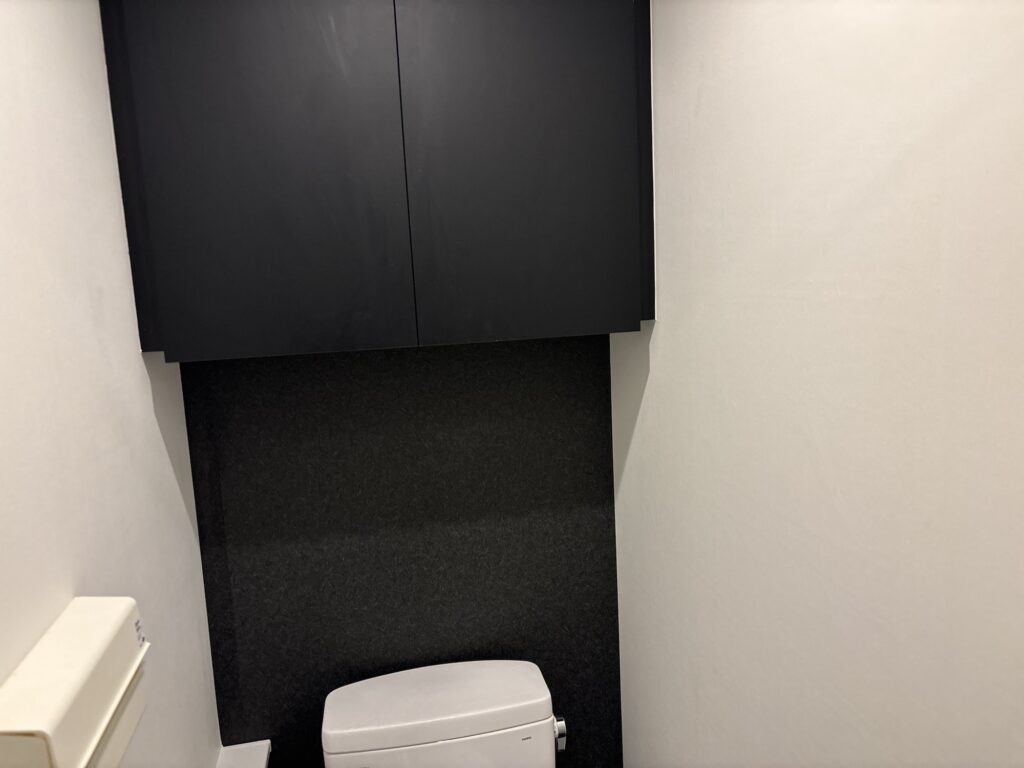 Finished black accent wallpaper covering the front wall of a commercial toilet after professional wallpaper installation.