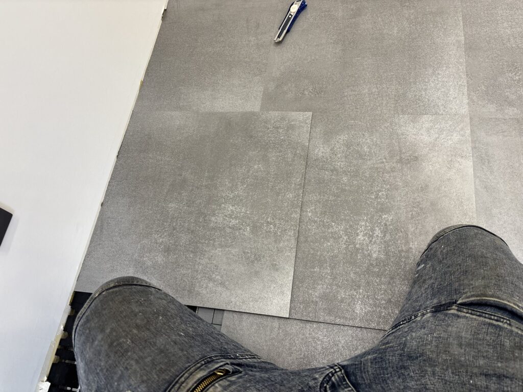 A full floor tile placed on top of another tile to mark the required cutting dimensions during a commercial flooring project.