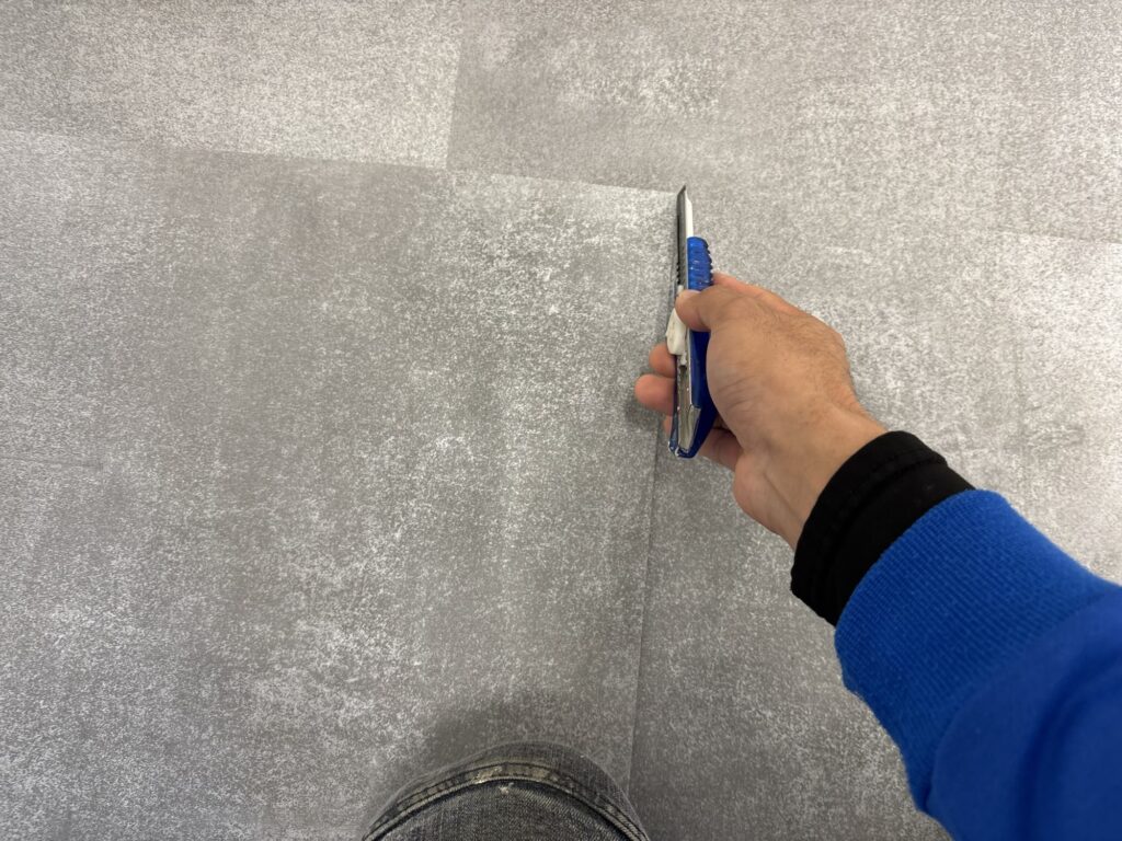 A worker using a full floor tile as a straightedge and reference guide while preparing a tile for cutting.