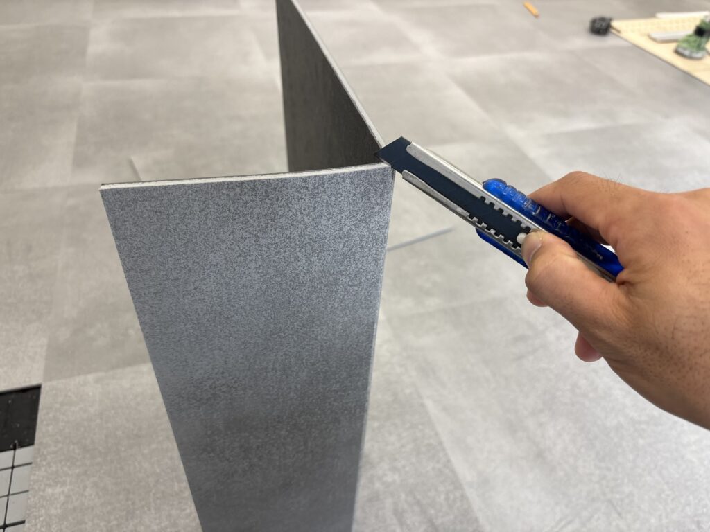 A worker scoring a floor tile with a utility knife before bending the material and completing the cut for a precise fit.