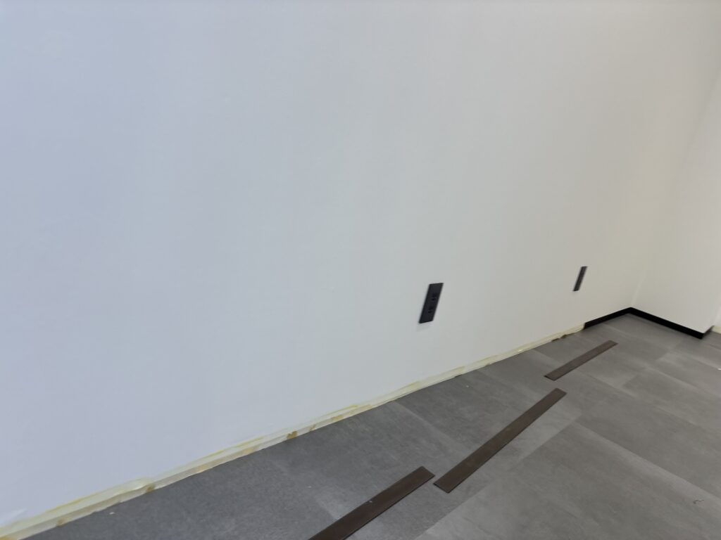 A worker fitting flexible soft baseboard material along the wall during the final stages of a commercial interior renovation.