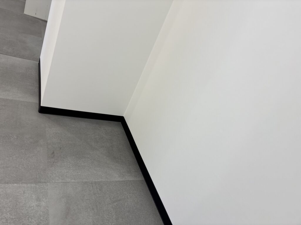 Finished soft baseboards installed along the wall and adjoining the newly installed floor tiles in a commercial room.
