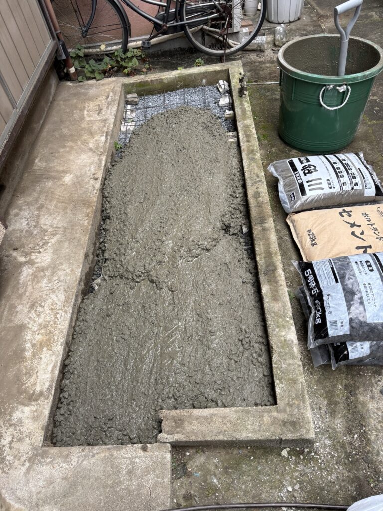 Fresh concrete being poured over the prepared base in front of a Japanese house.