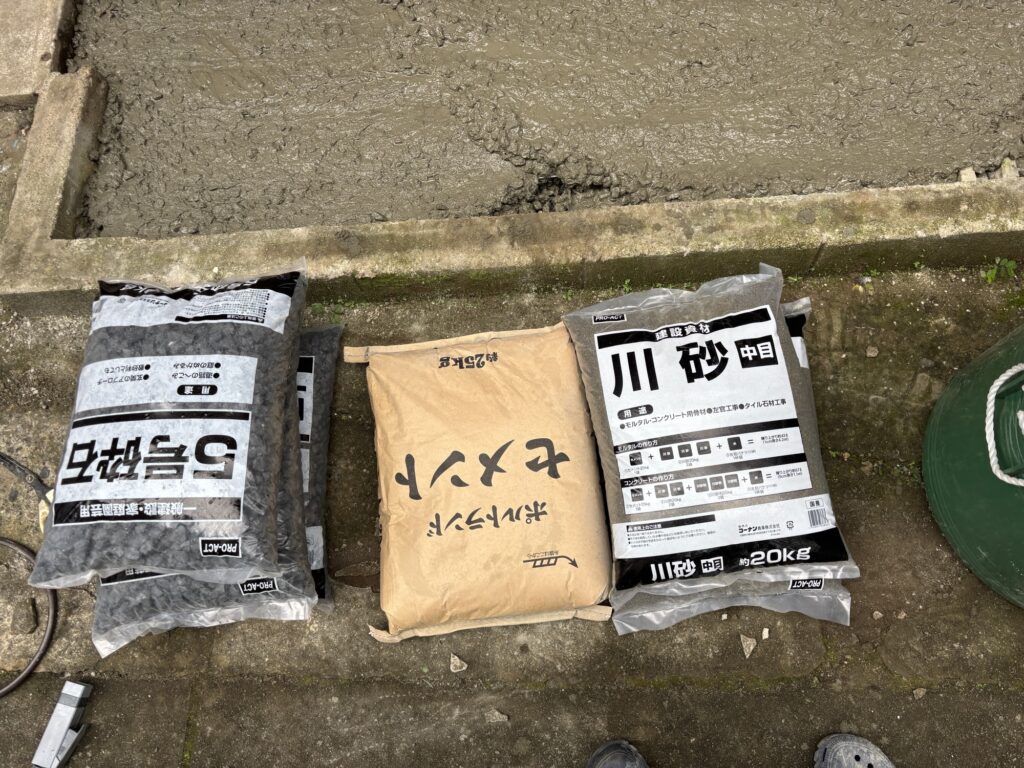 Bags of cement, river sand, and crushed stone prepared for a DIY concrete project.