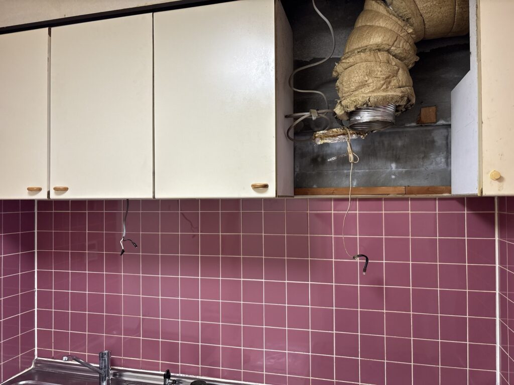 Kitchen wall and cabinet area after removal of the range hood and under-cabinet light during renovation.