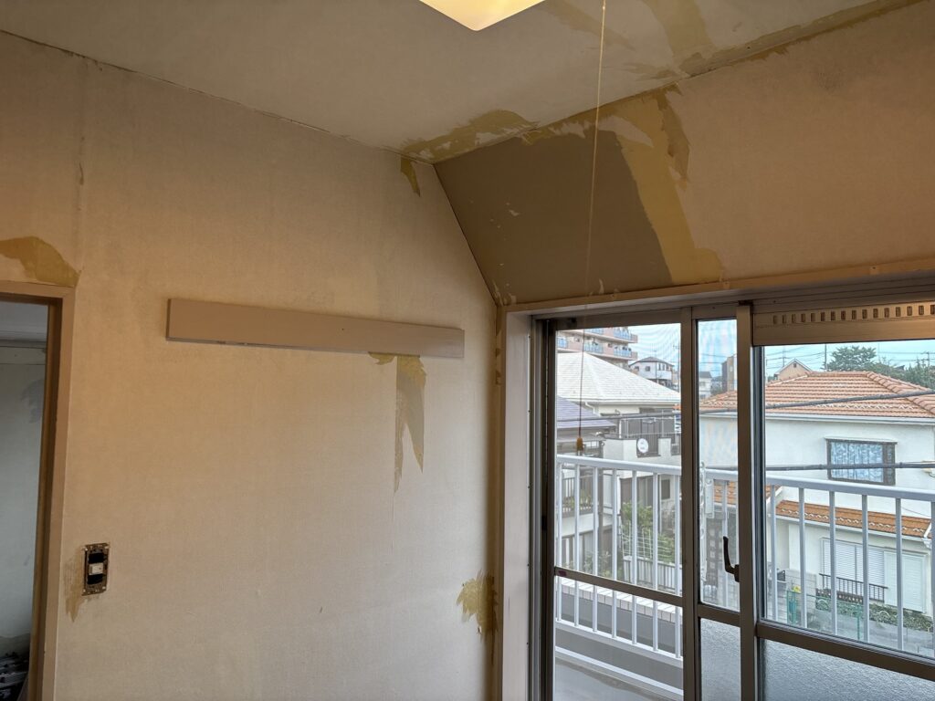 Interior wall showing the remaining wallpaper backing paper after stripping during apartment renovation work in Japan.